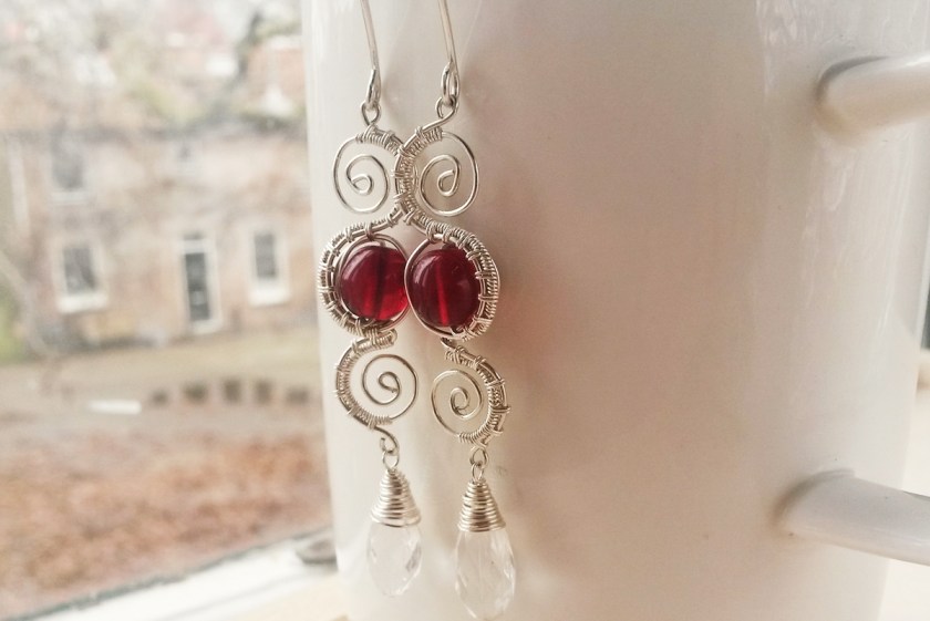 zilveren oorbellen met gewoven textuur, fijne spiralen en granaatrode glaskralen